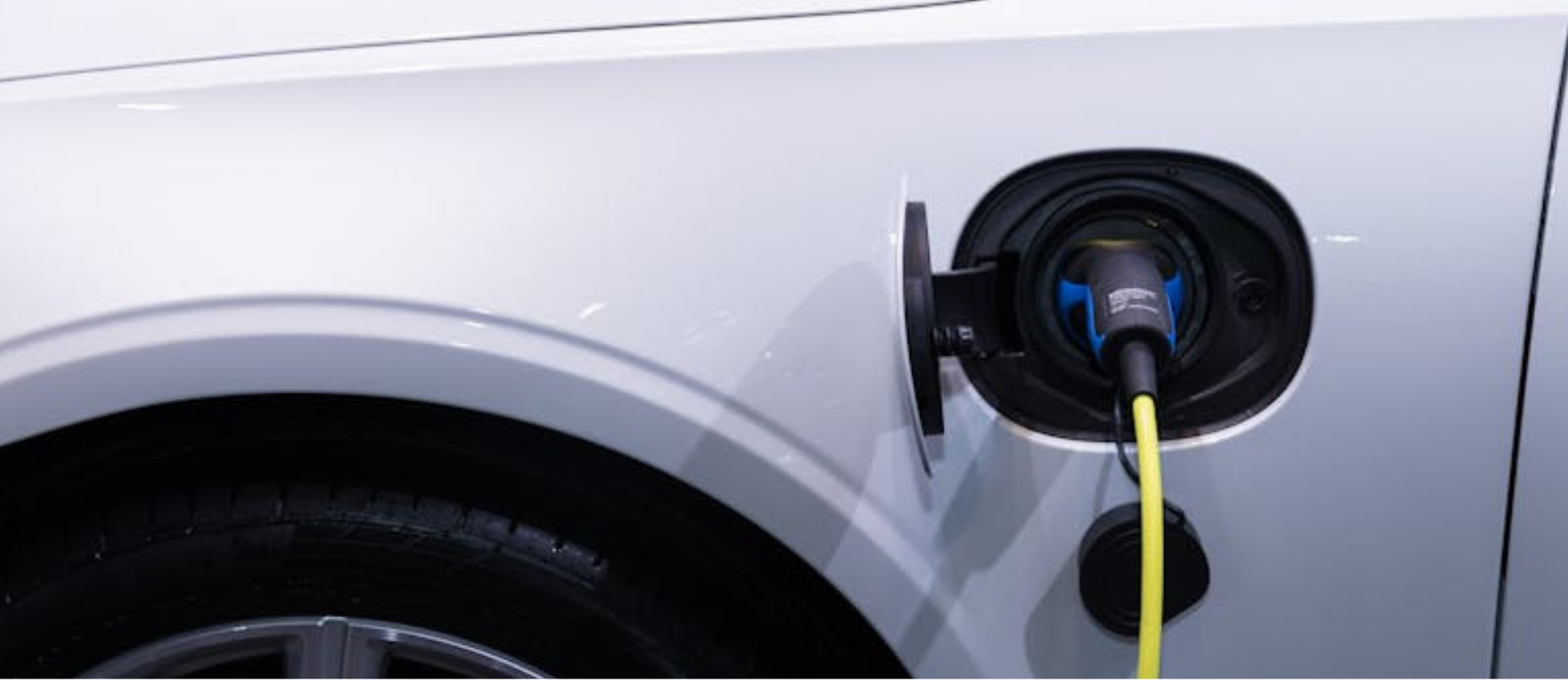 Vista lateral de un coche eléctrico blanco conectado a un punto de carga mediante un cable con conector